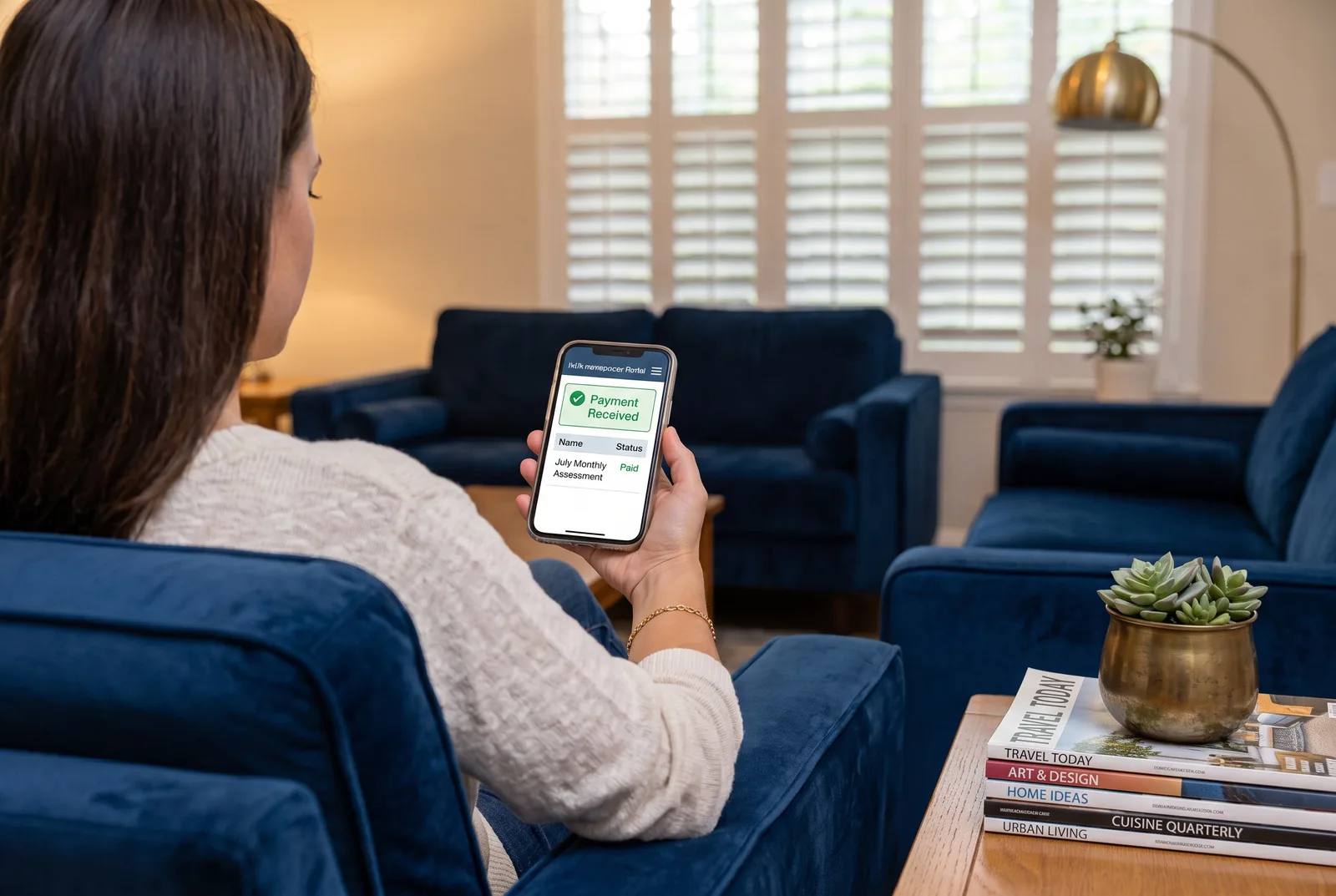 A homeowner paying their monthly HOA assessment online from the sofa, the portal showing a payment received confirmation